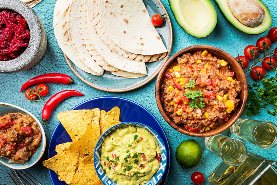 Mexican food mix: nachos, fajitas, tortilla, guacamole and salsa sauces and ingredients over blue background. Top view
